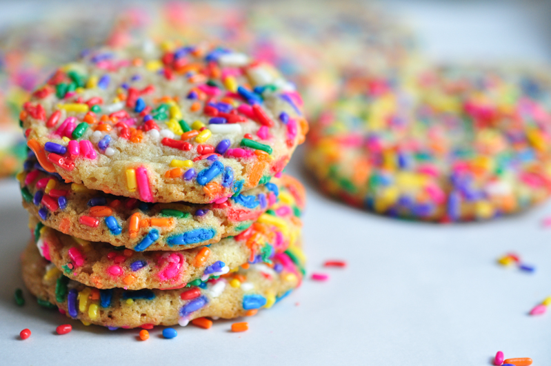 A stack of funfetti sugar cookies sits on a parchment lined baking tray. 