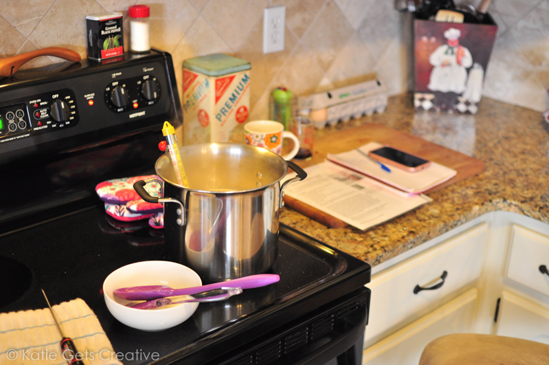 Cooking goat milk caramels in a stainless steel pot with a candy thermometer on a stovetop 