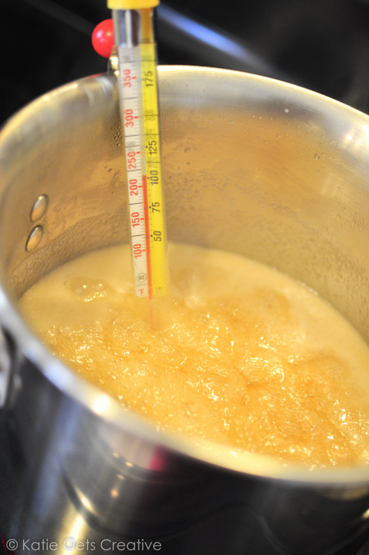 A pot of boiling caramel mixture with a candy thermometer clipped to the side