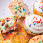 Funfetti Cupcakes on a white plate with one cupcake broken open to see the rainbow sprinkles inside.