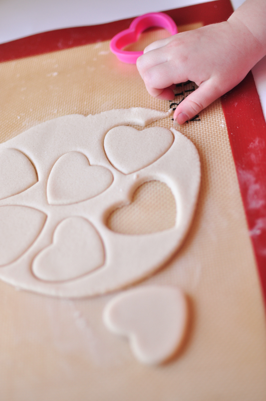 Child's hand cutting salt dough ornaments on a silicone baking mat