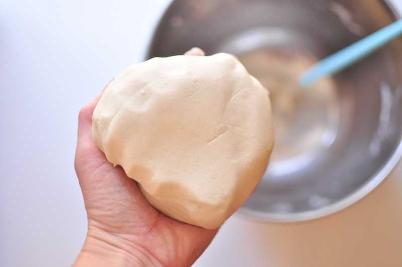 A ball of salt dough being held above a mixing bowl to show how the dough should appear