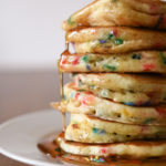 A stack of buttermilk pancakes with rainbow sprinkles and drizzled with syrup.