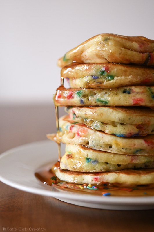 A stack of buttermilk pancakes with rainbow sprinkles and drizzled with syrup.