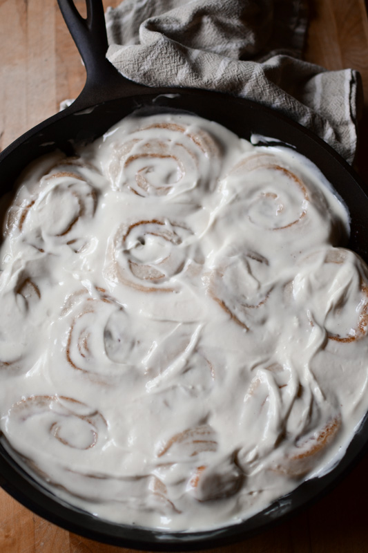 A cast iron skillet with iced sourdough cinnamon rolls
