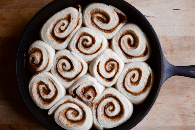 A cast iron skillet with baked sourdough cinnamon rolls, cooling and waiting to be frosted. 