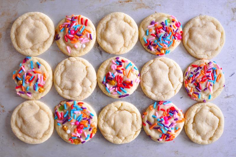 Chewy sugar cookies, half with sprinkles and half rolled in sugar on a baking pan
