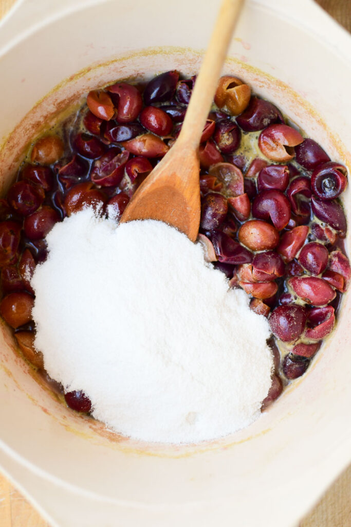 Adding sugar to a pan of muscadine hulls and juice to cook into a pie filling. 