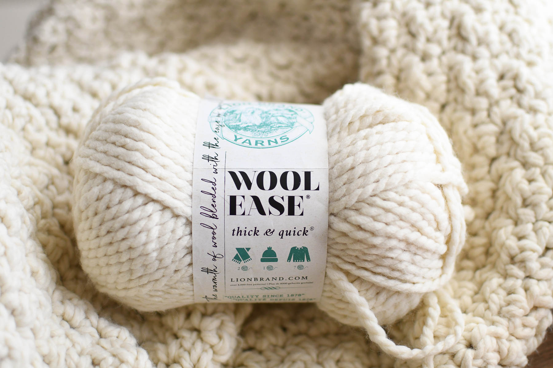 A ball of wool ease thick and quick yarn on a crochet blanket background.