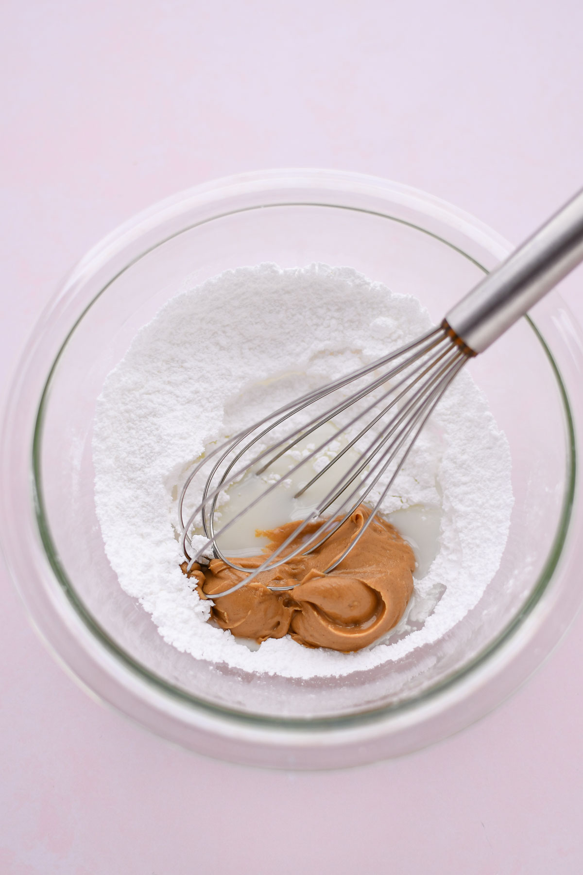 The ingredients for peanut butter icing in a small mixing bowl with a whisk. 