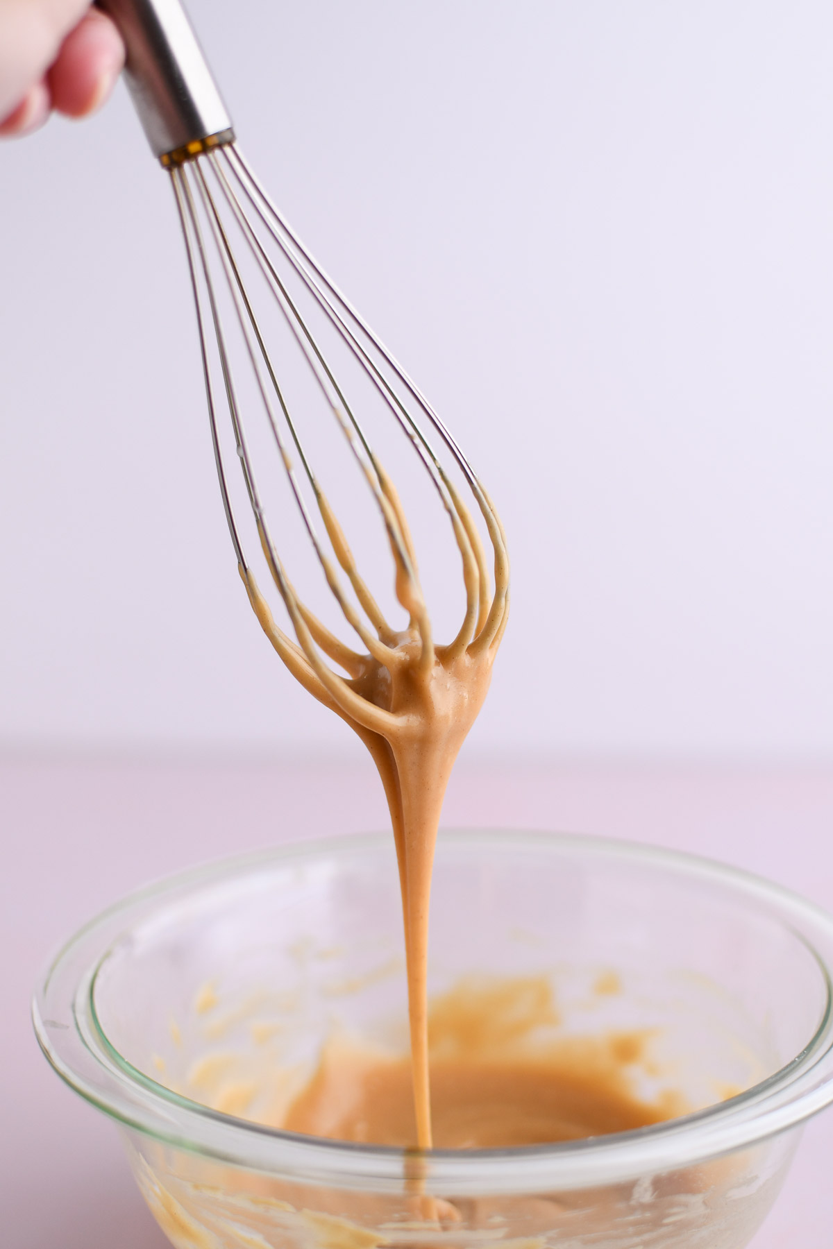 Icing dripping off of a whisk to show good consistency for drizzling. 