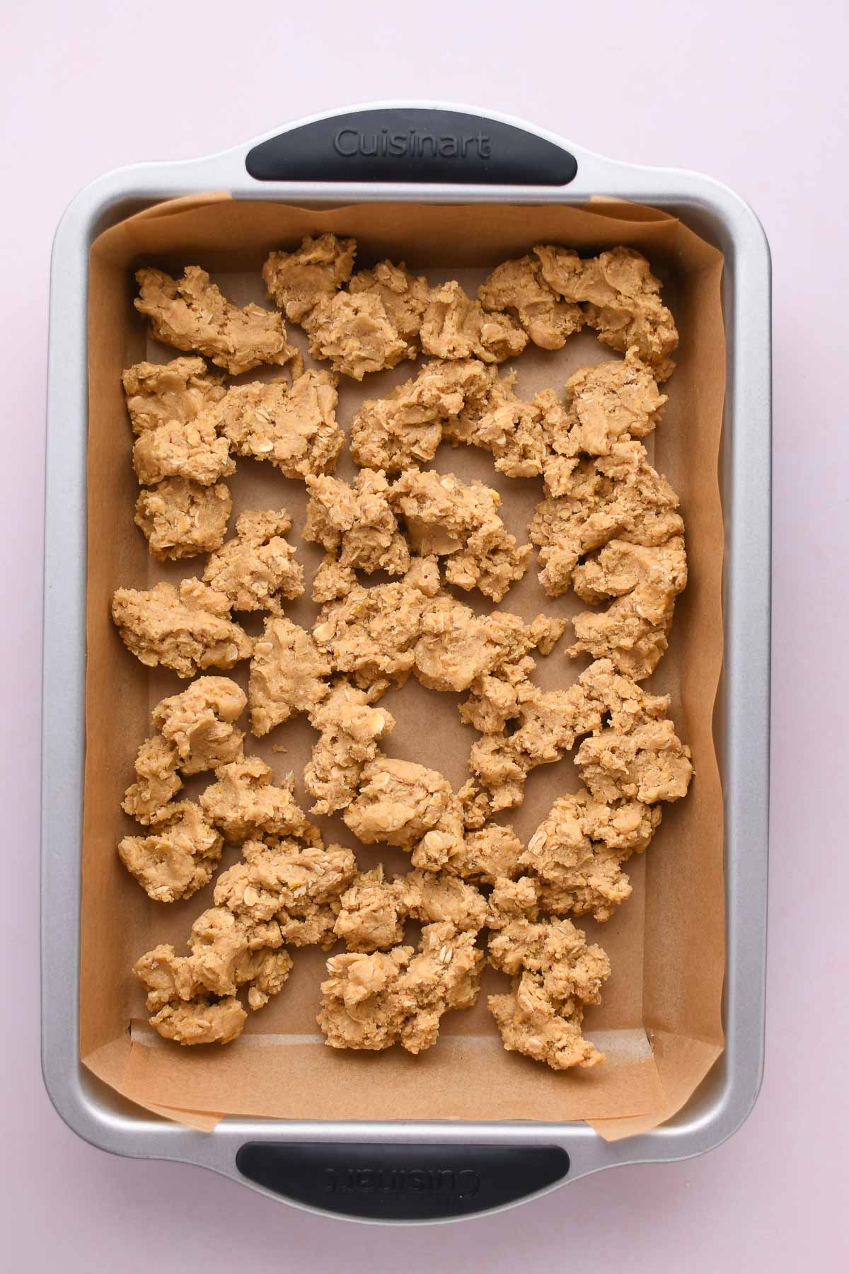 A parchment lined pan with clumps of cookie dough before spreading out.