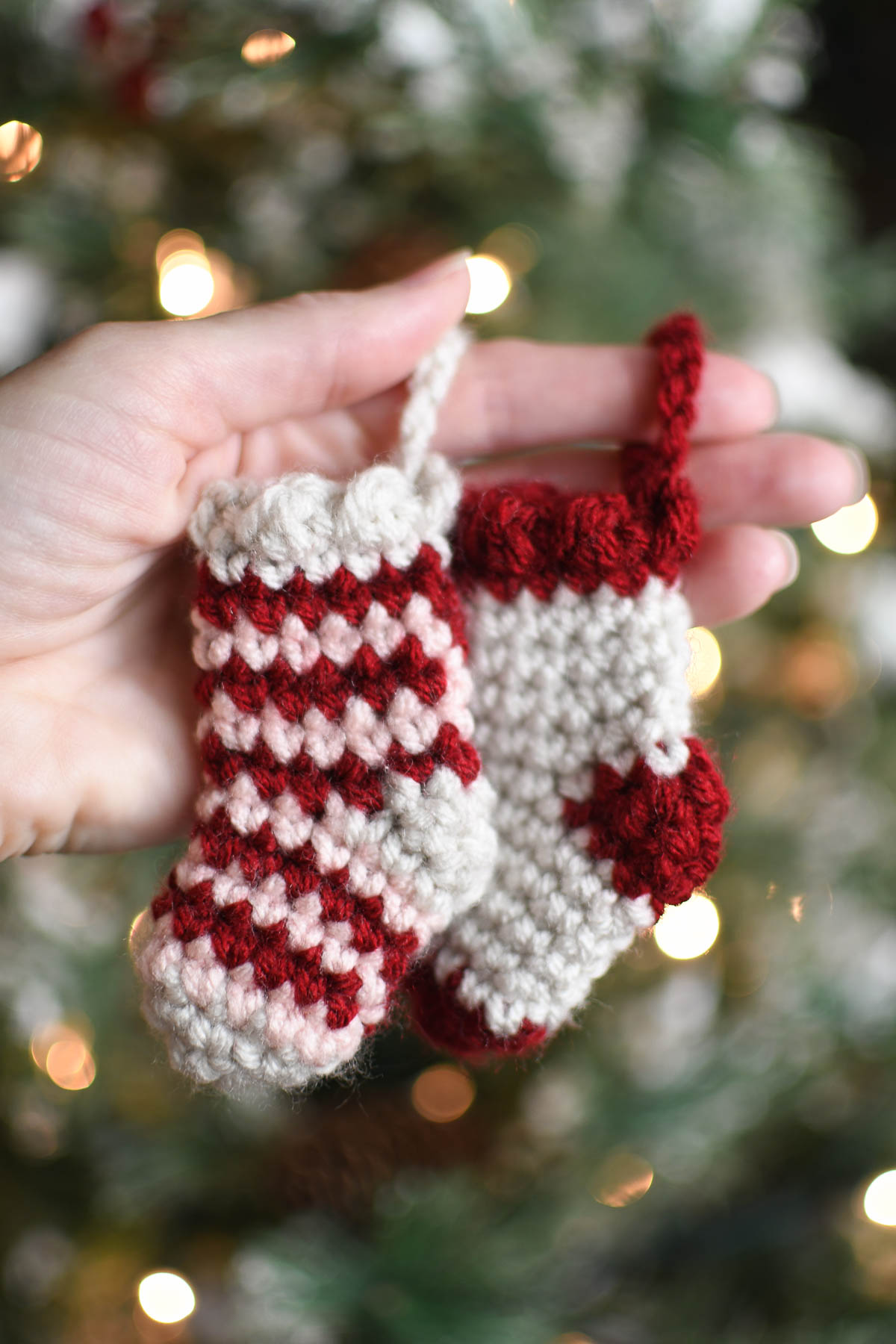 A hand holding 2 mini stockings looped around the index finger in front of a Christmas tree.